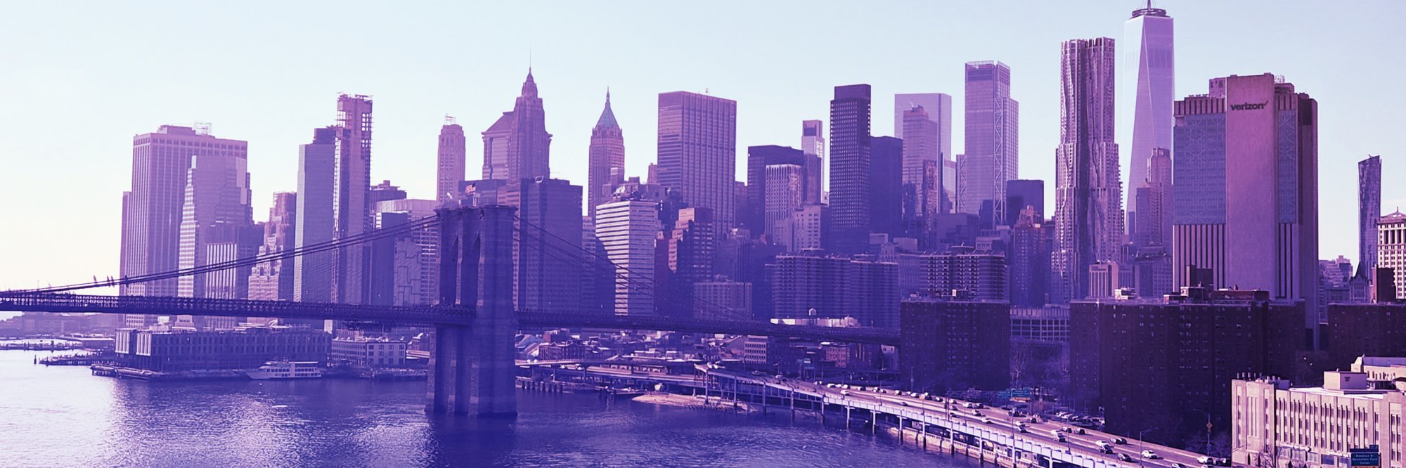 The skyscrapers of Lower Manhattan behind the Brooklyn Bridge, over the East River, in shades of purple.